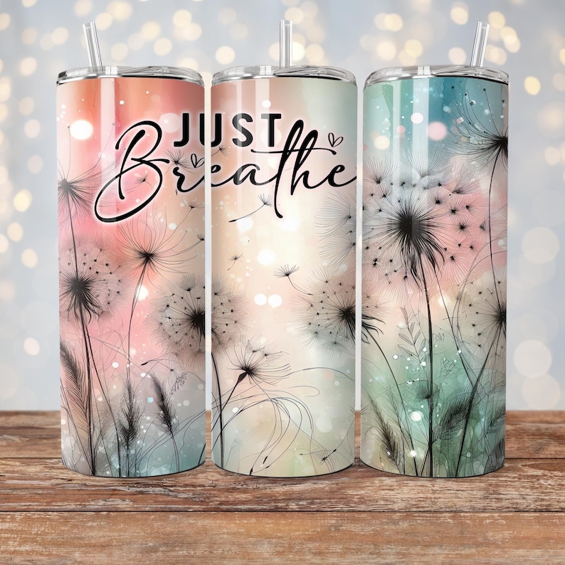 Op de afbeelding: Drie roestvrijstalen bekers met rietjes, elk met een ander pastel kleurenschema en een paardenbloem ontwerp. De woorden "JUST Breathe" zijn in zwart schrift op de voorkant van de bekers geschreven.