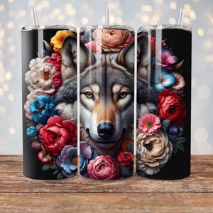 May include: A stainless steel tumbler with a black background and a wolf's face surrounded by colorful flowers. The wolf has gray fur and a brown nose. The flowers are red, pink, blue, and white.