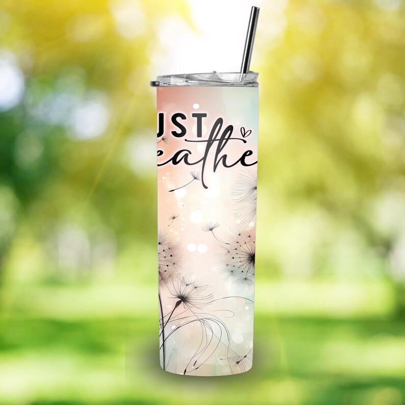 Op de afbeelding: Een roestvrijstalen beker met een rietje heeft de woorden "Just Breathe" in zwart schrift. De beker heeft een aquarelontwerp met perzik-, roze- en wittinten en zwarte paardenbloemillustraties.