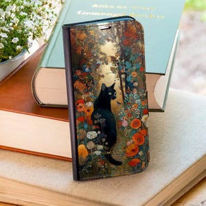 May include: A black phone case featuring a black cat in a colorful garden scene with flowers and butterflies. The case is open, revealing the phone's screen. The design has a vintage, artistic style, with a soft, painterly quality.