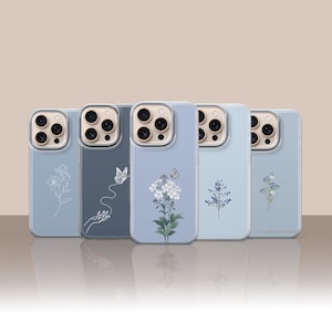 May include: Five smartphone cases in varying shades of blue, each featuring a unique botanical or butterfly illustration. The designs include white line art of flowers, a hand with a butterfly, a detailed floral cluster, and small blue sprigs.