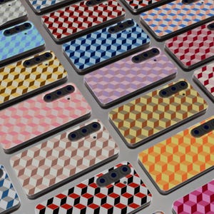 Puede incluir: Una colección de fundas para teléfonos inteligentes con patrones geométricos de cubos en varios colores, incluyendo rojo, azul, amarillo y rosa. Cada funda tiene un módulo de cámara con tres lentes.