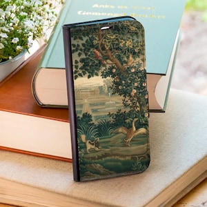 May include: A phone case with a landscape design featuring trees, birds, and a fountain. The case has a black border and a clasp. The design is in shades of green, beige, and brown, reminiscent of a tapestry.