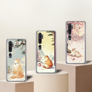 May include: Three phone cases with cat illustrations. One case features a ginger cat with a blue collar, another shows a cat near a tea cup, and the third depicts a cat under a cherry blossom tree. Each case has a clear border.
