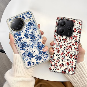 May include: Two phone cases with floral designs. One case features blue flowers on a white background, while the other showcases red flowers on a white background. Both cases have a clear border and a camera lens cutout.