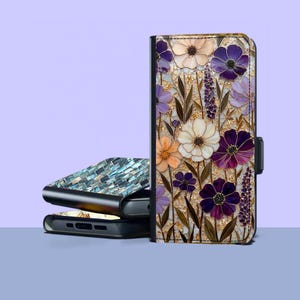 Pode incluir: Uma capa de telemóvel retangular com um design de mosaico floral com flores brancas, roxas e cor de laranja sobre um fundo com salpicos dourados. Uma segunda capa é visível ao fundo, exibindo um padrão de azulejos retangulares azuis e verde-azulados.