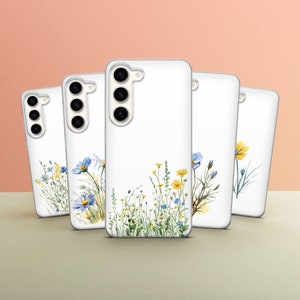 Puede incluir: Cuatro fundas para teléfono con fondo blanco y diseño floral. Las flores son azules, amarillas y verdes. Las fundas tienen la parte posterior transparente y una protuberancia de cámara elevada.