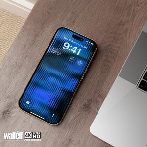 May include: A gold smartphone with a blue and black patterned screen displaying the time 9:41 AM. The phone is on a wooden surface next to a silver laptop.