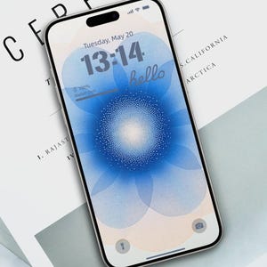 May include: A smartphone displaying a blue and white abstract design with a digital clock showing 13:14 and the word "hello". The date is Tuesday, May 20. The phone is on a white surface with the word "CEREAL" printed on it.