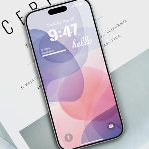 以下が含まれることがあります： 画面にピンクとパープルの抽象的なデザインが施されたスマートフォン。時間は9:47で、日付は5月20日火曜日。画面には「hello」というテキストが表示されています。