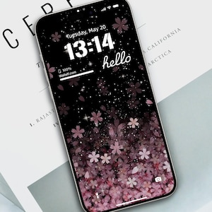 Könnte beinhalten: Ein schwarzer Telefonbildschirm mit einem rosa-weißen Blumenmuster. Die Uhrzeit ist 13:14 Uhr und der Tag ist Dienstag, der 20. Mai. Der Text "hello" wird auf dem Bildschirm angezeigt.