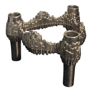 May include: A silver-colored, three-stem candle holder with a textured, organic design. The candle holder has three cylindrical openings for candles and three supporting legs. The design is reminiscent of a mountain range.