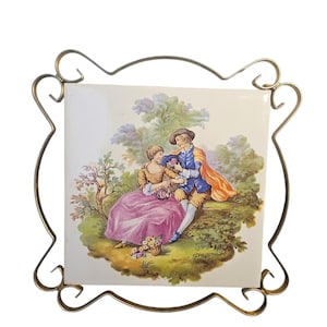 Könnte beinhalten: Dekorative Fliese mit einer romantischen Gartenszene eines Paares, eingefasst in einem goldfarbenen Metallrahmen. Die Fliesenkunst zeigt einen Mann und eine Frau mit einem Blumenkorb. Das Kunstwerk ist mit "Fragonard" signiert.