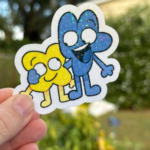 May include: A glittery sticker featuring two cartoon characters, a blue '4' and a yellow 'X', both with smiling faces and black outlines. The blue character has a wide grin, and the sticker is held against a blurred green background.