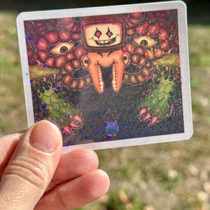 May include: Square sticker featuring a colorful illustration of a video game scene. The artwork depicts a large, menacing creature with a television screen face, large teeth, and multiple eyes. A small character stands in front of the creature. The sticker has a glittery finish.