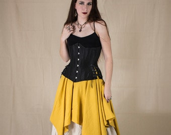 May include: A black corset with a lace-up back is worn over a black top. The corset is paired with a mustard-yellow asymmetrical skirt and a cream-colored skirt underneath. The outfit is completed with black sandals.