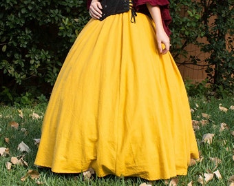 May include: A Renaissance-style outfit featuring a burgundy off-the-shoulder top with bell sleeves, a black corset, and a full, golden-yellow skirt. The ensemble is set against a backdrop of green foliage and grass.