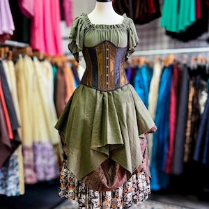 May include: A green and brown corset dress on a mannequin. The dress features a ruffled neckline, a fitted corset with brown and black panels, and a layered skirt with a skull print at the hem. The dress is displayed in a clothing store.