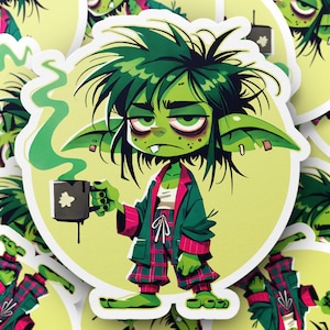 Peut inclure: Une créature verte ressemblant à un gobelin avec des cheveux verts et de grandes oreilles porte un pyjama à carreaux verts et rouges et tient une tasse de café fumante. La créature a une expression fatiguée et est entourée de fumée verte.