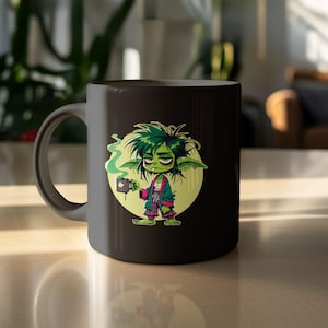 May include: Black ceramic mug featuring a cartoon goblin character with green hair and skin, wearing a robe and holding a coffee cup. The goblin is set against a yellow circle, with green steam rising from the cup. The mug is on a light-colored surface.