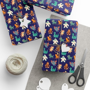 May include: Wrapped gifts with navy blue paper featuring a colorful pattern of cartoon monsters. Each package is tied with twine and a decorative tag. A ball of twine, scissors, and blank tags are also visible.