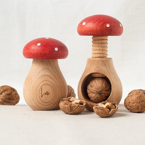Op de afbeelding: Twee houten notenkrakers in de vorm van rode en witte paddenstoelen met witte stippen. De grotere notenkraker heeft een walnoot in het kraakmechanisme. De kleinere notenkraker heeft het woord "Lotte" gegraveerd op de zijkant.