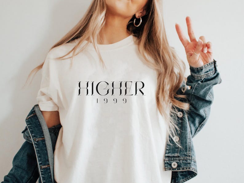 Peut inclure: Un t-shirt blanc avec le texte "HIGHER 1999" imprim&eacute; en noir.