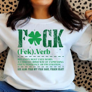May include: White sweatshirt with a green graphic that reads "F*CK" with a shamrock, and the definition of the word. The text also includes "Ireland's most used word" and other related terms.