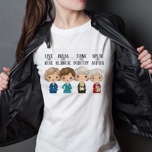 Puede incluir: Camiseta blanca con una ilustración de dibujos animados de cuatro mujeres y el texto "LIVE LIKE ROSE, DRESS LIKE BLANCHE, THINK LIKE DOROTHY, SPEAK LIKE SOPHIA." Las mujeres visten diferentes atuendos.