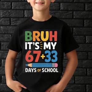 May include: Black t-shirt with a colorful graphic that reads "BRUH IT'S MY 67+33 DAYS OF SCHOOL" with a blue pencil illustration. The text is in various colors, including green, yellow, red, and blue.