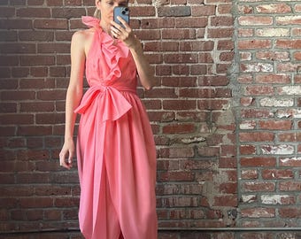 May include: A pink halter dress with a ruffled neckline and a bow at the waist. The dress is made of a lightweight fabric and has a flowing skirt.