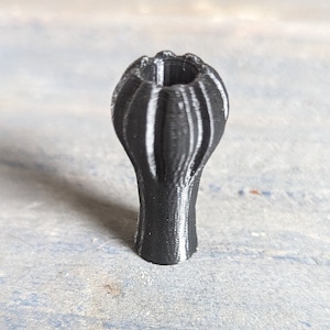 May include: A black 3D printed vase with a ribbed design. The vase has a wide opening at the top and a narrow base.