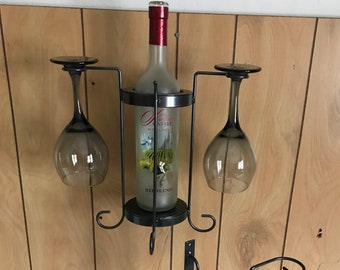 May include: A black metal wine rack with two glass holders and a bottle holder. The rack is mounted on a wall. The wine bottle is labeled "Old Castle Riesling".
