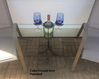 May include: A black metal wine bottle and glass holder with two blue wine glasses. The holder has a central compartment for a wine bottle and two side holders for glasses. The holder is on a three-legged stand.