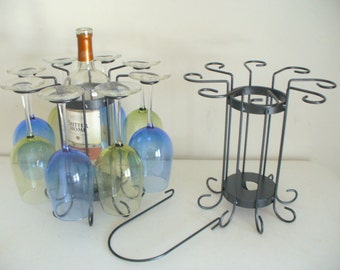 May include: A black metal wine rack with a bottle of wine and six wine glasses. The rack has a circular base and a cylindrical center with a removable top. The glasses are blue and green.