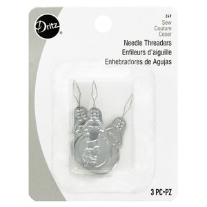 May include: A package of three silver needle threaders. The package has the brand name "Dritz" and the text "Needle Threaders" in English, French, and Spanish. The threaders are designed for sewing and couture.