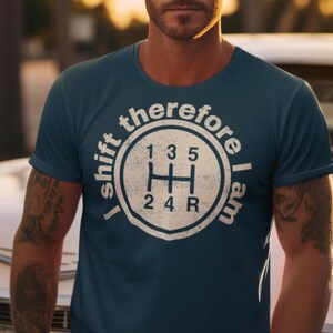 May include: A navy blue t-shirt with a white graphic of a car's gear shift and the text "I shift therefore I am". The graphic includes the numbers 1, 3, 5, 2, 4, and R.