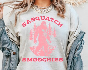 May include: A light gray sweatshirt with a pink graphic of a sasquatch holding a cup with the text "Sasquatch Smoochies".