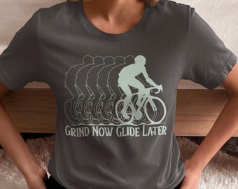 Könnte beinhalten: Ein dunkelgraues T-Shirt mit einem Grafikdruck eines Radfahrers auf einem Fahrrad. Die Grafik wird mehrmals wiederholt und erzeugt so einen Bewegungseffekt. Der Text "Grind Now Glide Later" ist unterhalb der Grafik aufgedruckt.