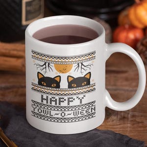 Può includere: Tazza in ceramica bianca con un motivo a maglia bianco e nero con due gatti neri che spuntano da dietro il design. Il testo "Happy Yowl-o-Ween" è stampato in nero sulla tazza.