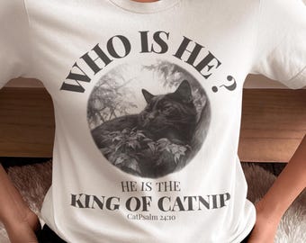 May include: White t-shirt with a black and white graphic of a cat inside a circle, with the text "WHO IS HE?" above and "HE IS THE KING OF CATNIP" below. The shirt also includes the text "CatPsalm 24:10".