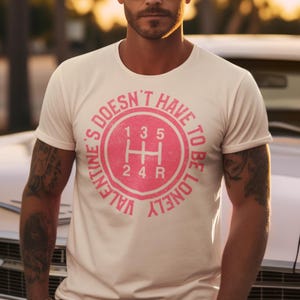 Pode incluir: Camiseta branca com um gráfico rosa de um padrão de mudança de marcha de um carro. O gráfico diz "Valentine's Doesn't Have To Be Lonely".
