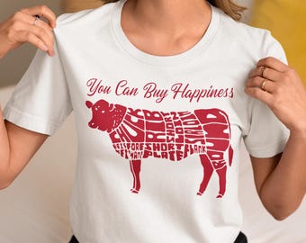 Puede incluir: Camiseta blanca con un gráfico rojo de una vaca con las palabras "You Can Buy Happiness" y los diferentes cortes de carne etiquetados en la vaca.