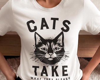 Könnte beinhalten: Weißes T-Shirt mit einem schwarzen Katzen-Gesicht-Motiv und dem Text "CATS TAKE WHAT THEY PLEASE". Das Katzendesign hat einen Spritzeffekt. Das Shirt hat einen Rundhalsausschnitt und kurze Ärmel.