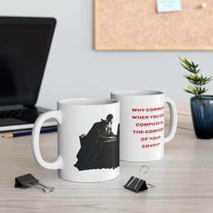May include: Two white coffee mugs with a black and white illustration of a person working on a laptop. The mug on the right has the text "WHY COMMUTE WHEN YOU CAN COMPUTE IN THE COMFORT OF YOUR CRYPT?" in red.