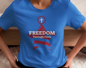 Puede incluir: Una camiseta azul con un diseño de estrella roja, blanca y azul. La estrella tiene una cruz dentro de un círculo en la parte superior y las palabras "FREEDOM Through Faith" debajo.