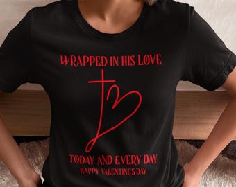 May include: Black t-shirt with red text that reads "Wrapped in His Love" with a red cross and heart design. The text "Today and Every Day" and "Happy Valentine's Day" are also printed in red.