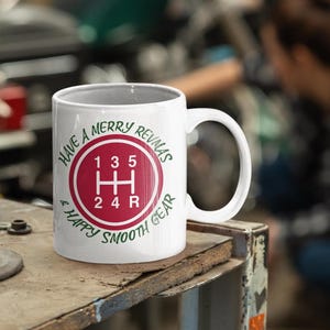 May include: White ceramic mug with a red and green gear shift pattern and the text "Have a Merry Revmas & Happy Smooth Gear".