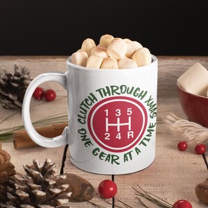 Könnte beinhalten: Eine weiße Keramiktasse mit einem roten und grünen Design. Das Design zeigt ein Schaltmuster mit dem Text "One gear at a time, clutch through Xmas".
