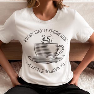 Könnte beinhalten: Weißes T-Shirt mit schwarzer Grafik einer Kaffeetasse mit Dampf. Der Text lautet: "EVERY DAY I EXPERIENCE - A LITTLE deJAVA VU - ".